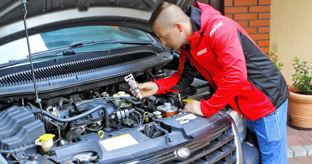 mężczyzna z preparatem do uszczelniania przekładni kierowniczych w dłoni pochyla się nad silnikiem