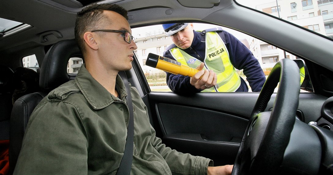 mężczyzna za kierownicą testowany przez policjanta alkomatem AlcoBlow