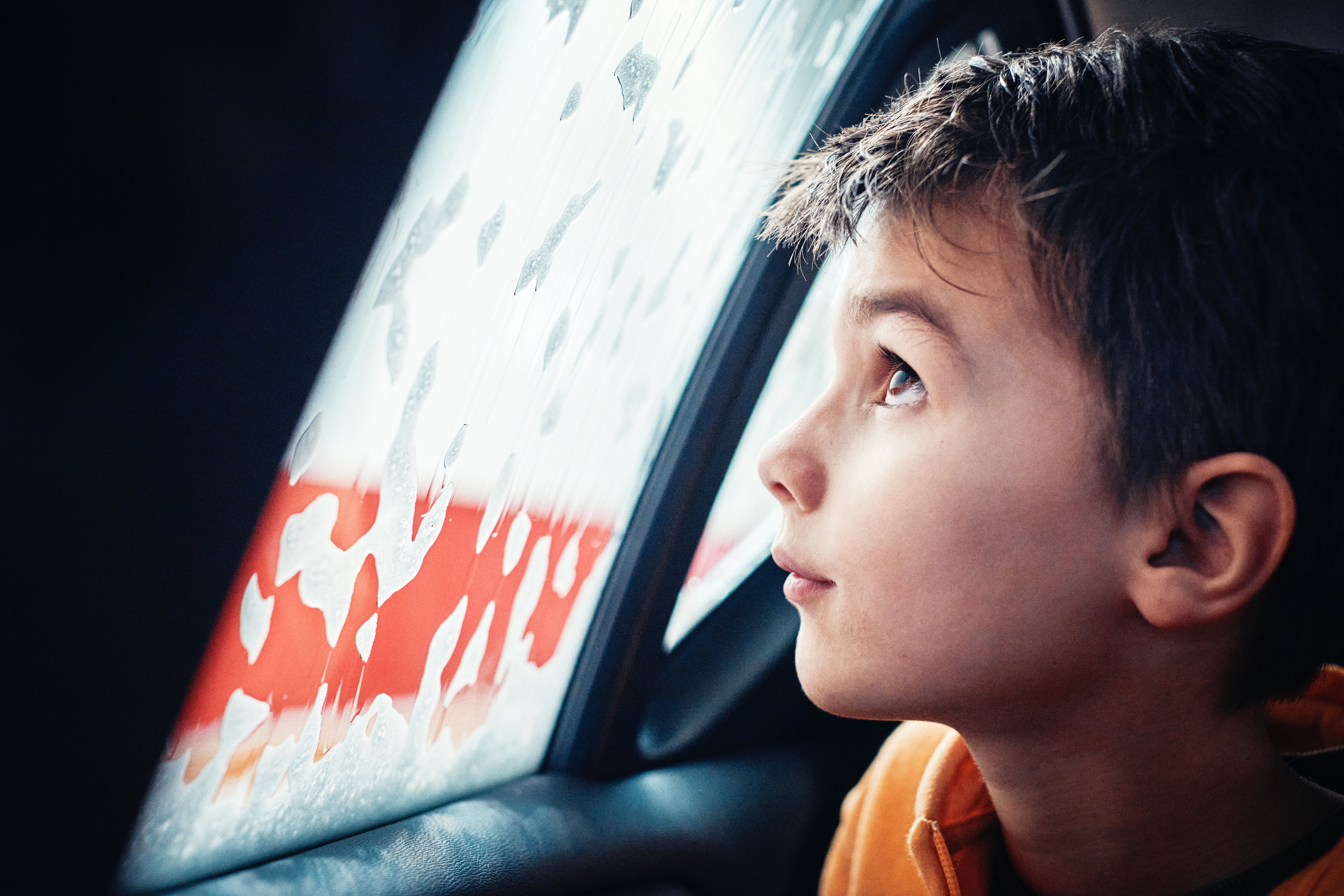 dziecko w samochodzie wygląda przez mokrą szybę