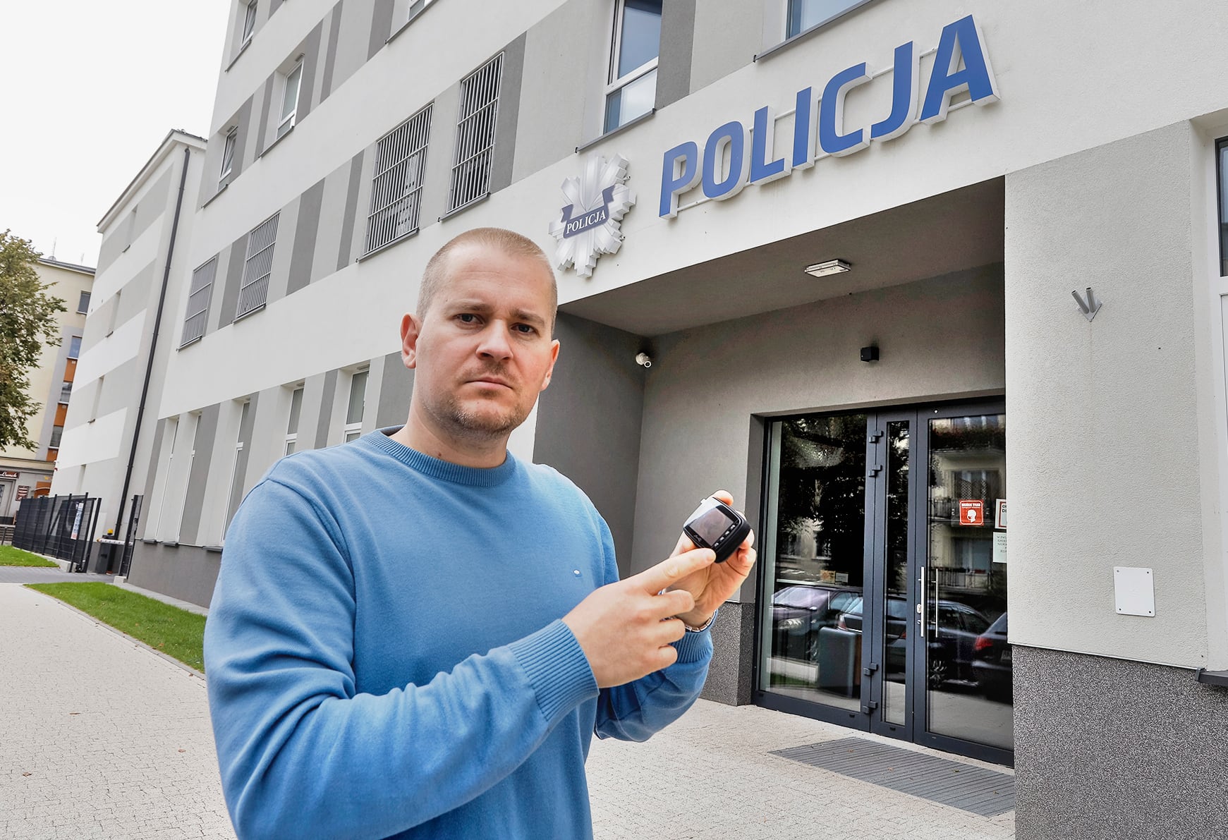 mężczyzna z kamerą pokładową w dłoni przed posterunkiem policji