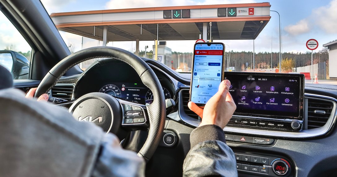 kierowca w samochodzie przed bramką na autostradzie z telefonem z aplikacją eTOLL