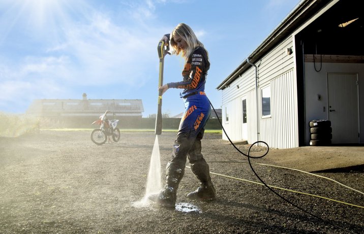 kobieta w kombinezonie wyścigowym opłukuje buty myjką wysokociśnieniową