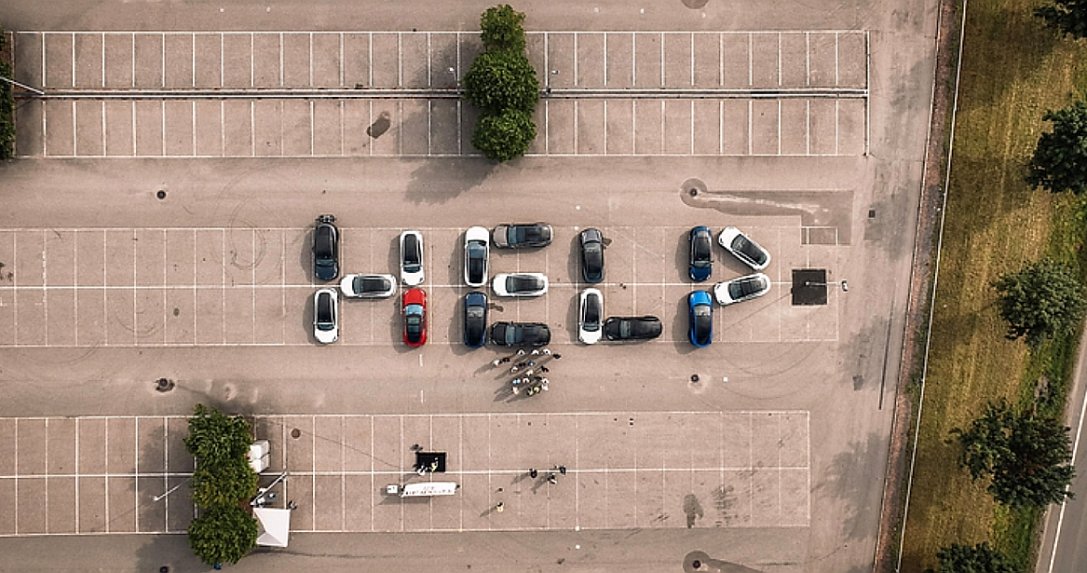 napis "HELP" ułożony na parkingu z samochodów