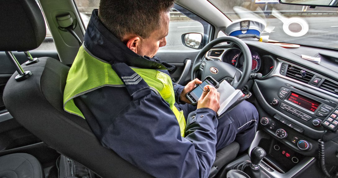 policjant w radiowozie sprawdza dane kierowcy przed wypisaniem mandatu