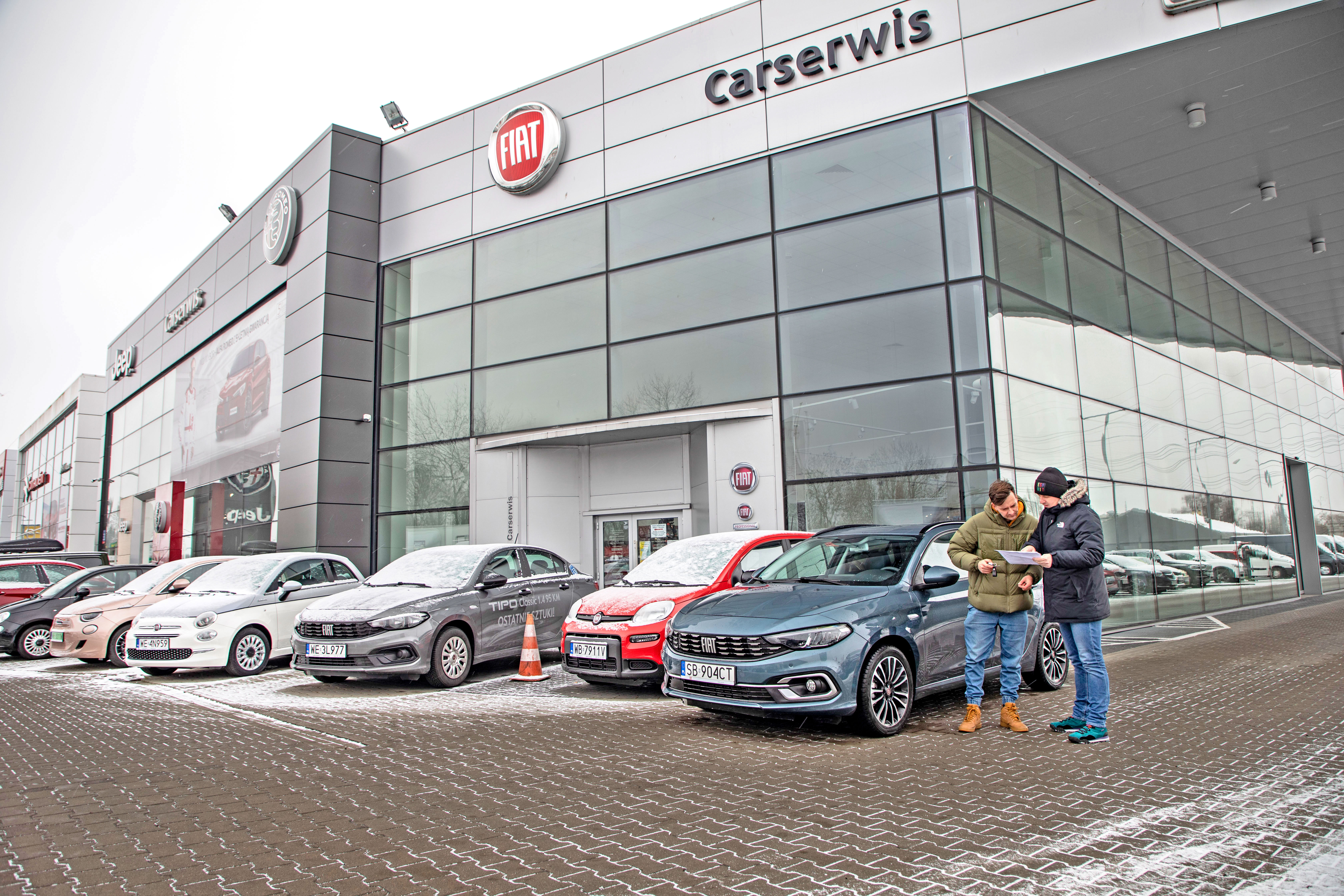 mezczyzni przed salonem sprzdaży rozmawiają z dokumentem w reku