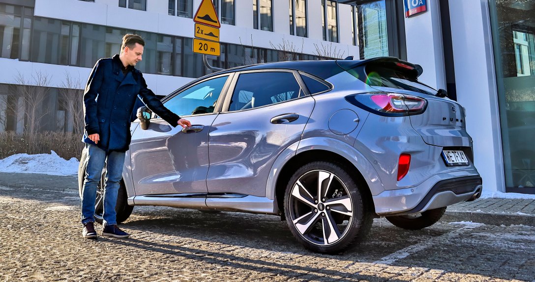 kierowca wsiada do auta służbowego zaparkowanego pod biurowcem