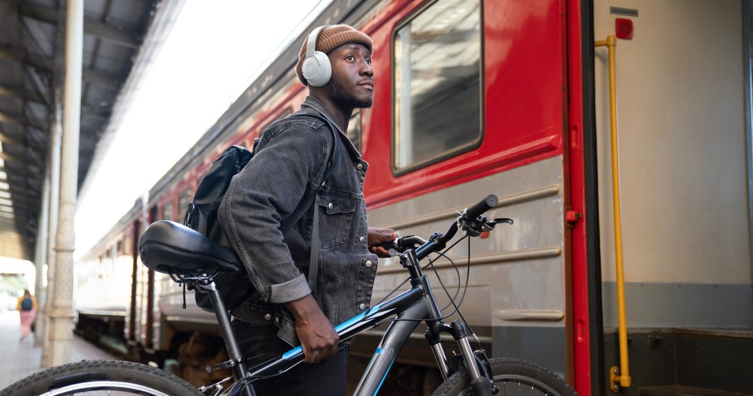 Słuchawki JBL Tune 770 NC – mężczyzna w słuchawkach z rowerem na dworcu kolejowym