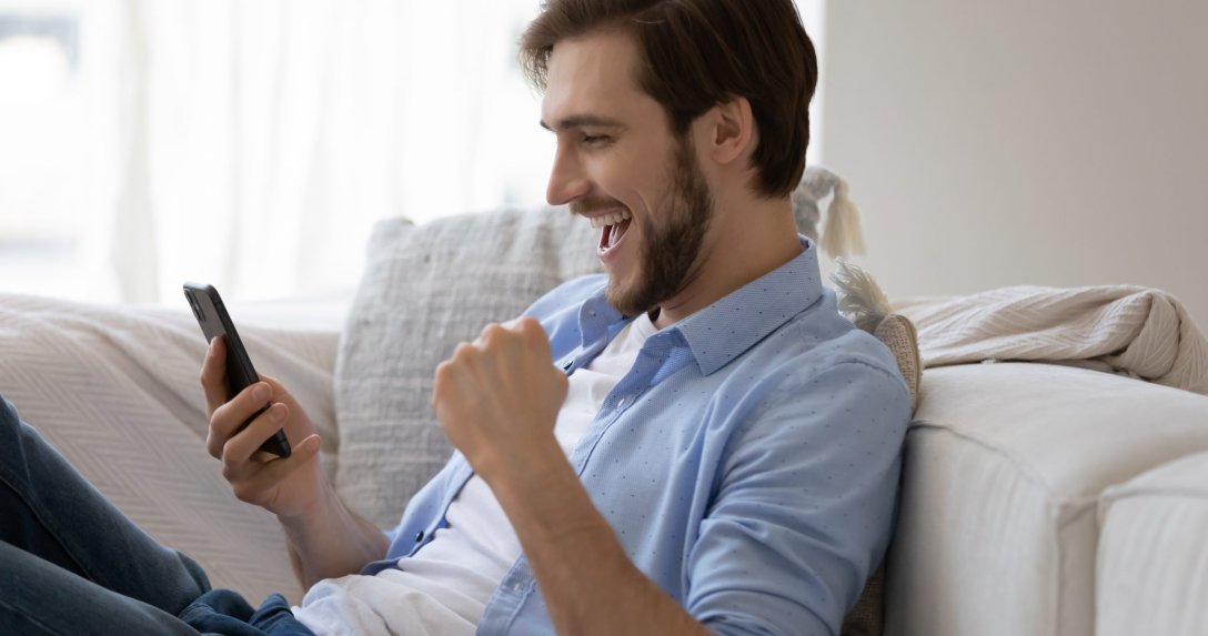mężczyzna patrzący na ekran smartfonu – na twarzy i w gestach satysfakcja i radość