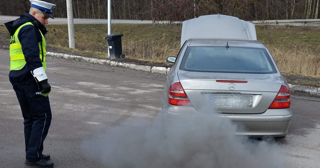 policjant stojący przy Mercedesie z dymiącą rurą wydechową