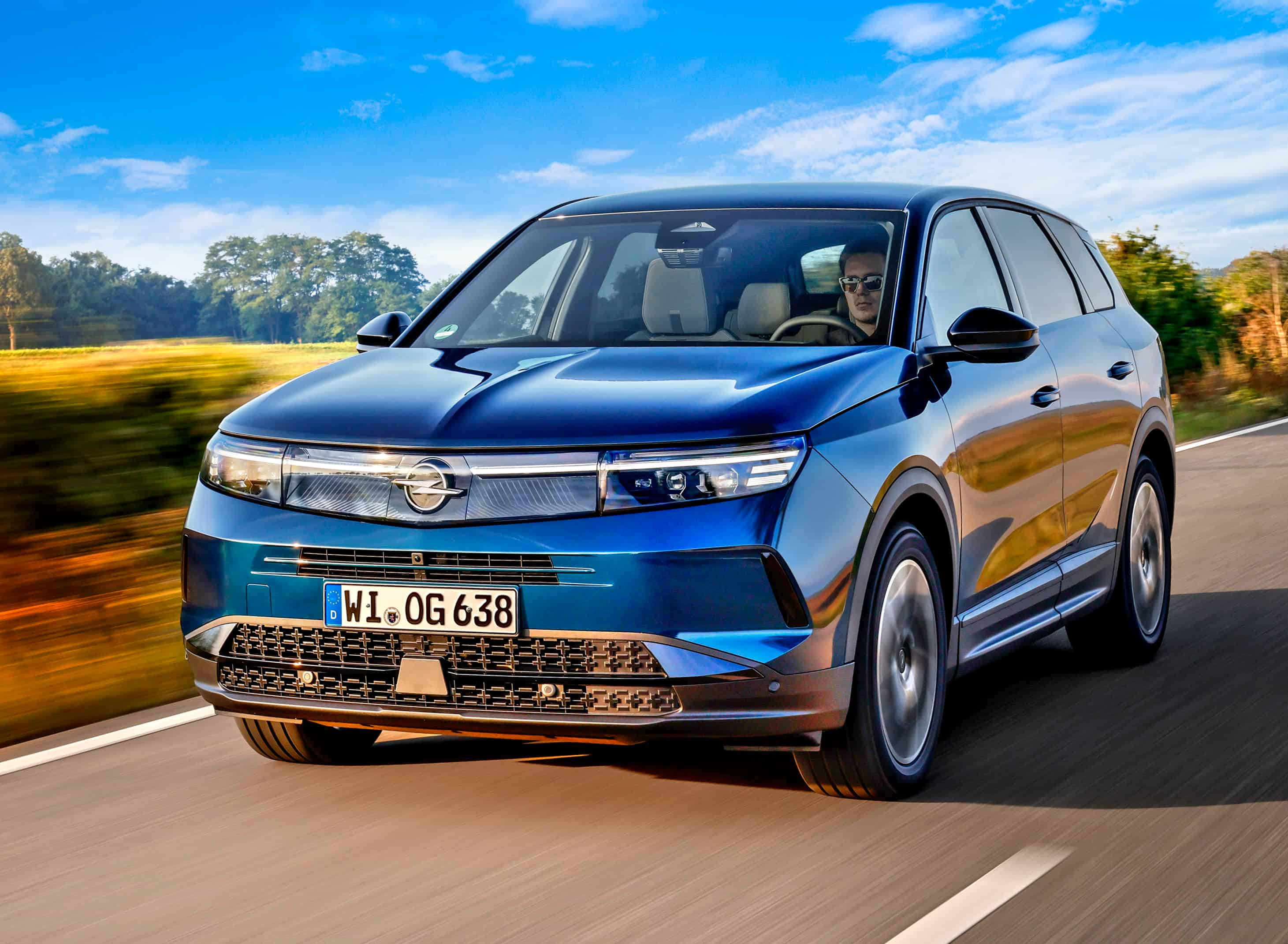 Opel Grandland Hybrid w niebieskim lakierze podczas jazdy, ujęcie z przodu i boku.