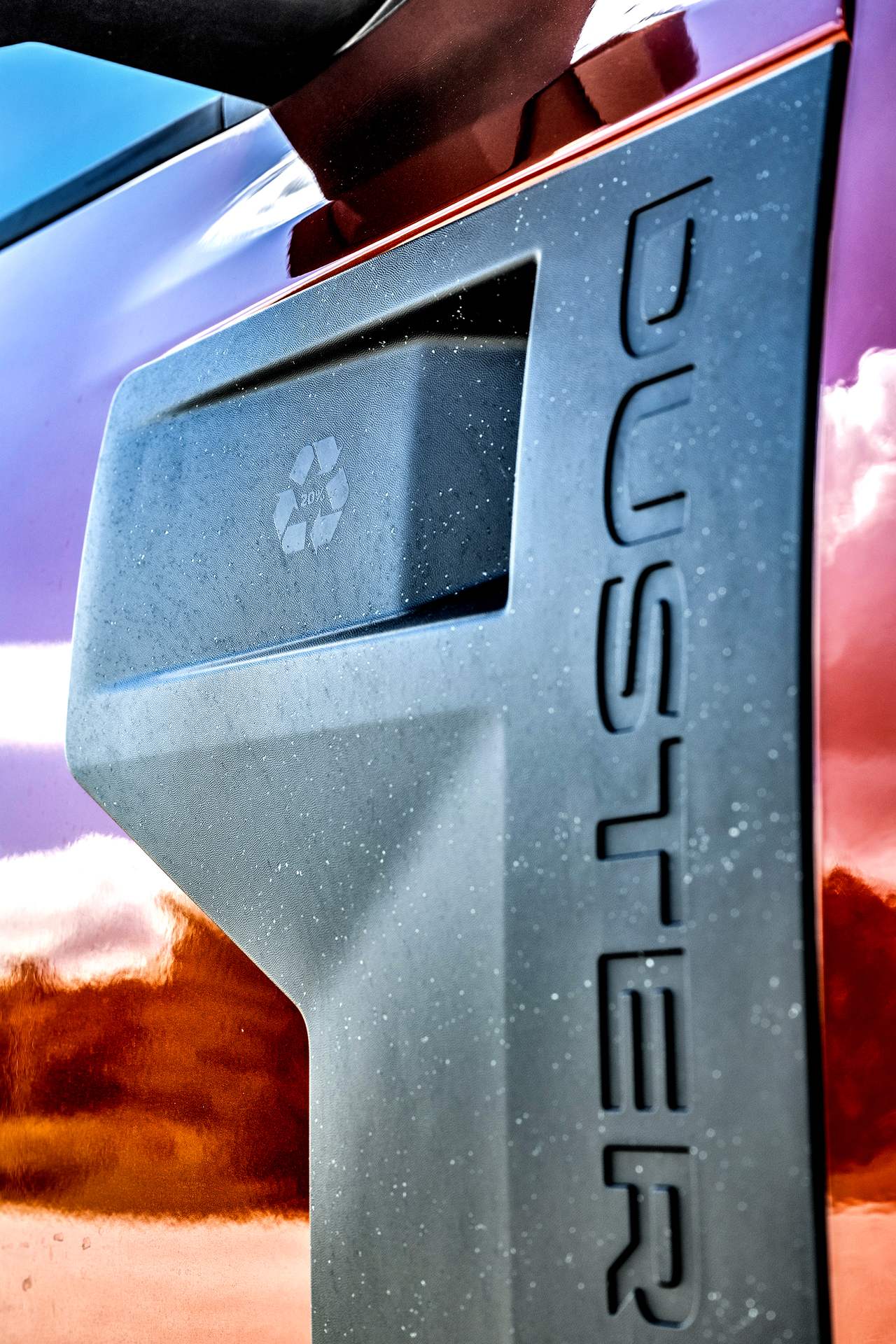 Zbliżenie na nielakierowany element nadwozia Dacii Duster III z tworzywa Starkle i wytłoczonym napisem Duster